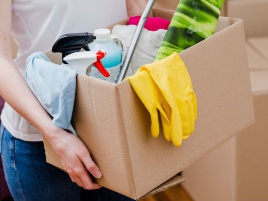 woman holding card board box and cleaning supplies